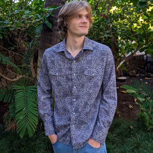 Man wearing a patterned shirt standing outdoors with greenery around