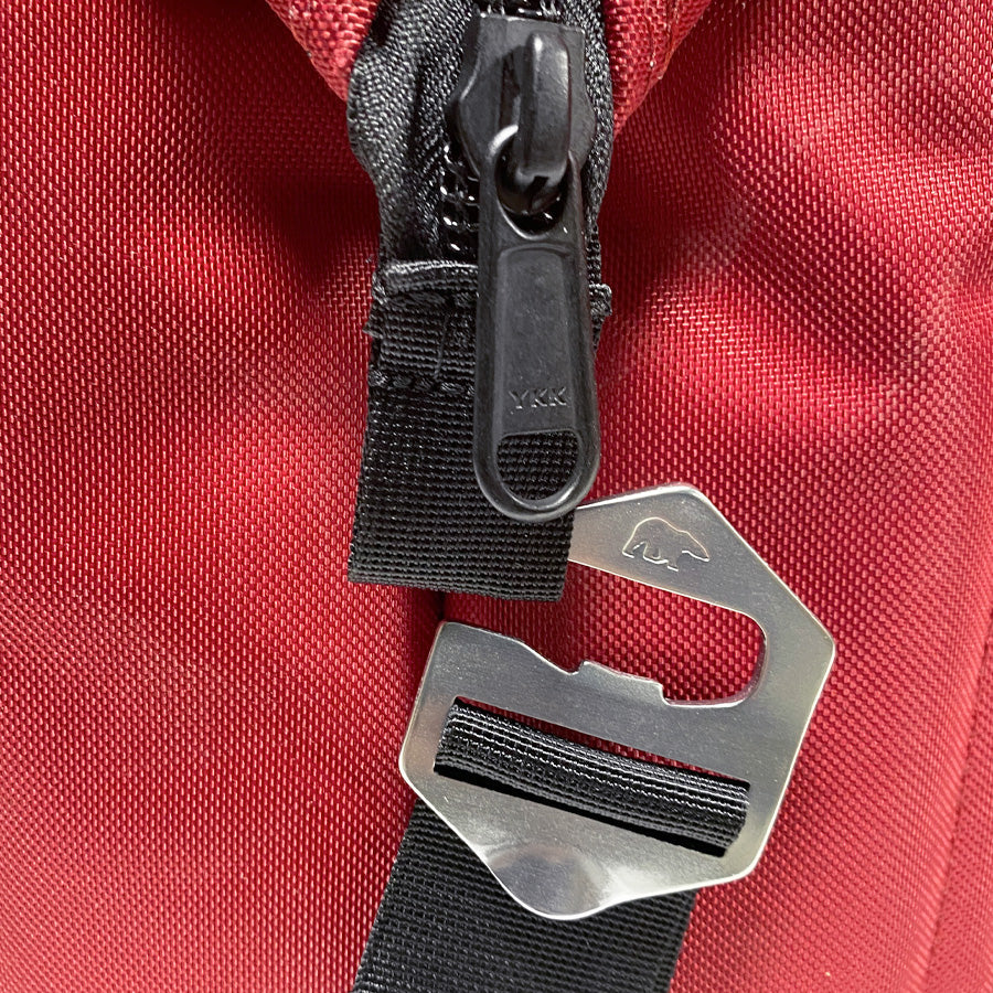 Close-up of a red bag with a black zipper and metal clasp on a red background