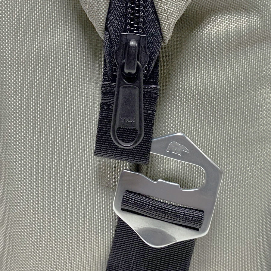 Close-up of a black zipper and metal buckle on a beige fabric background