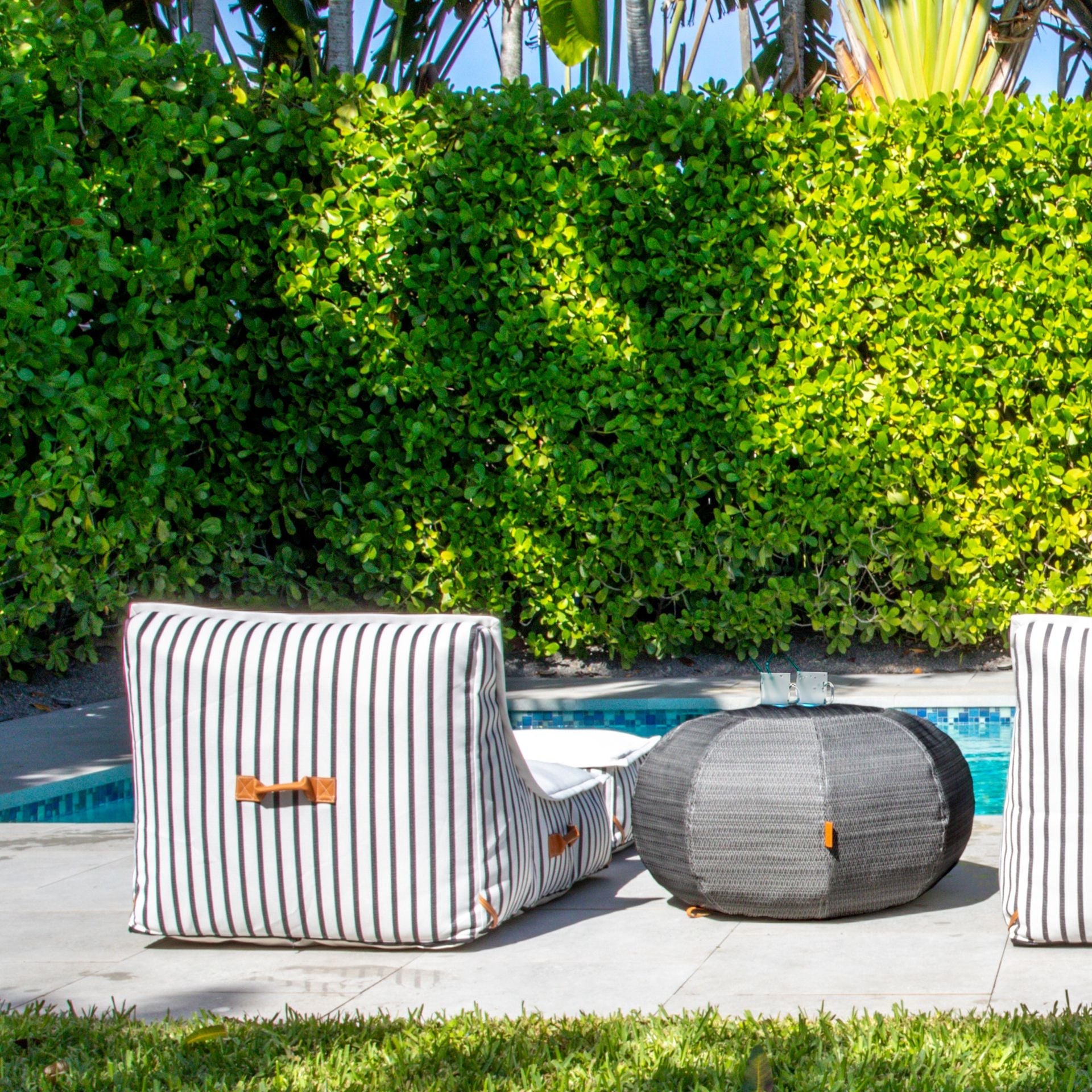 Striped outdoor chairs by a pool with greenery in the background