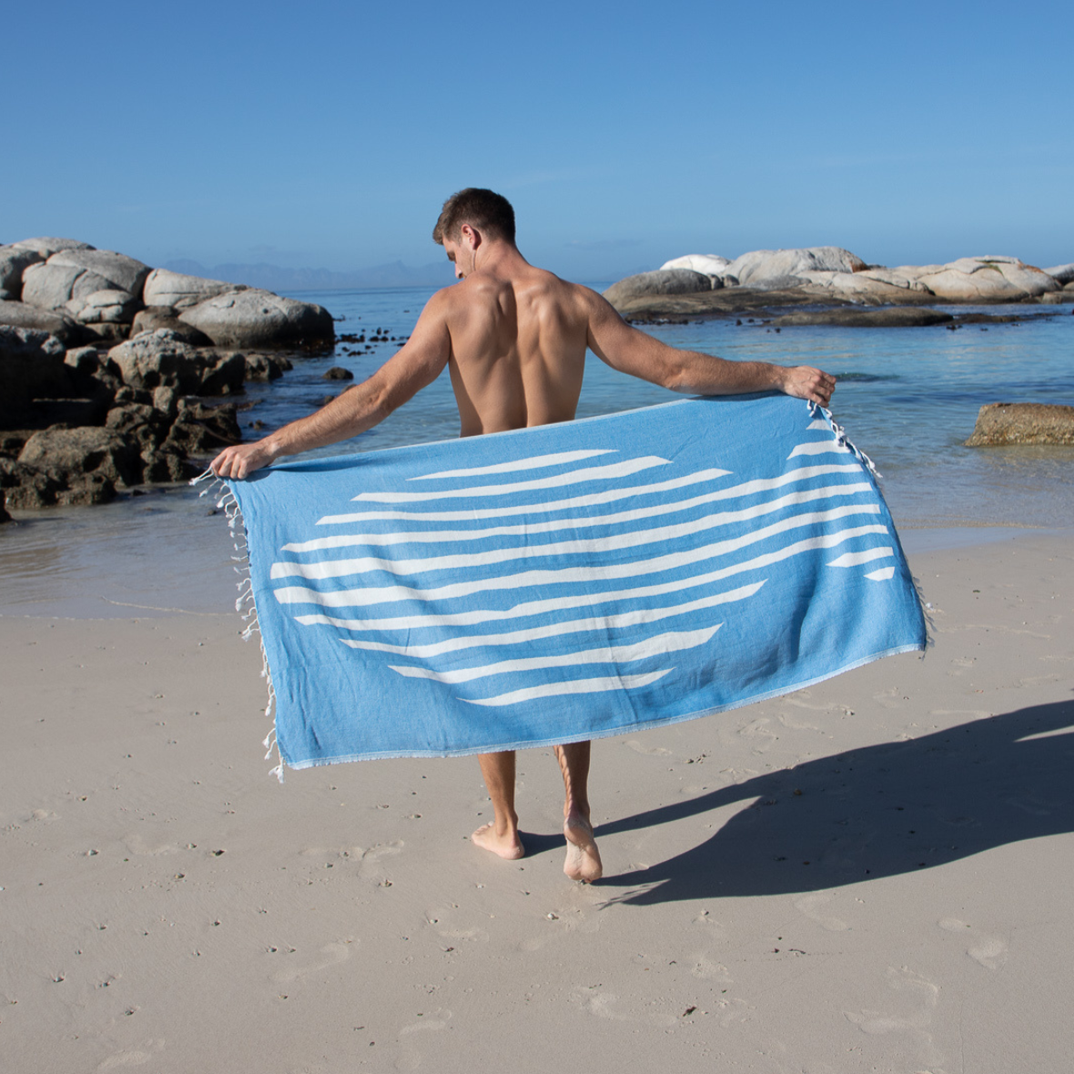 Man holding a blue and white striped towel on a beach