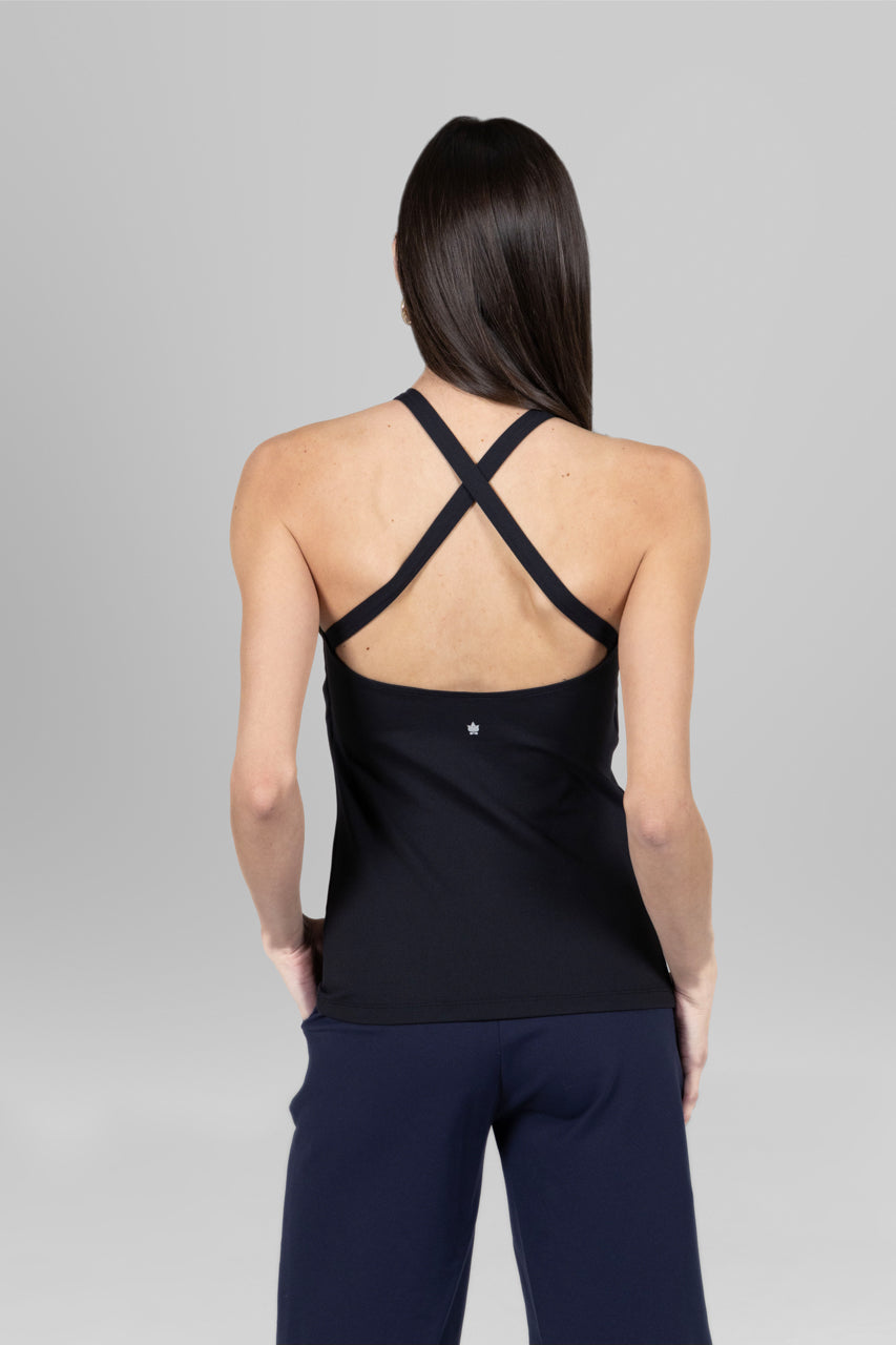 Person wearing a black tank top with criss-cross straps on a gray background