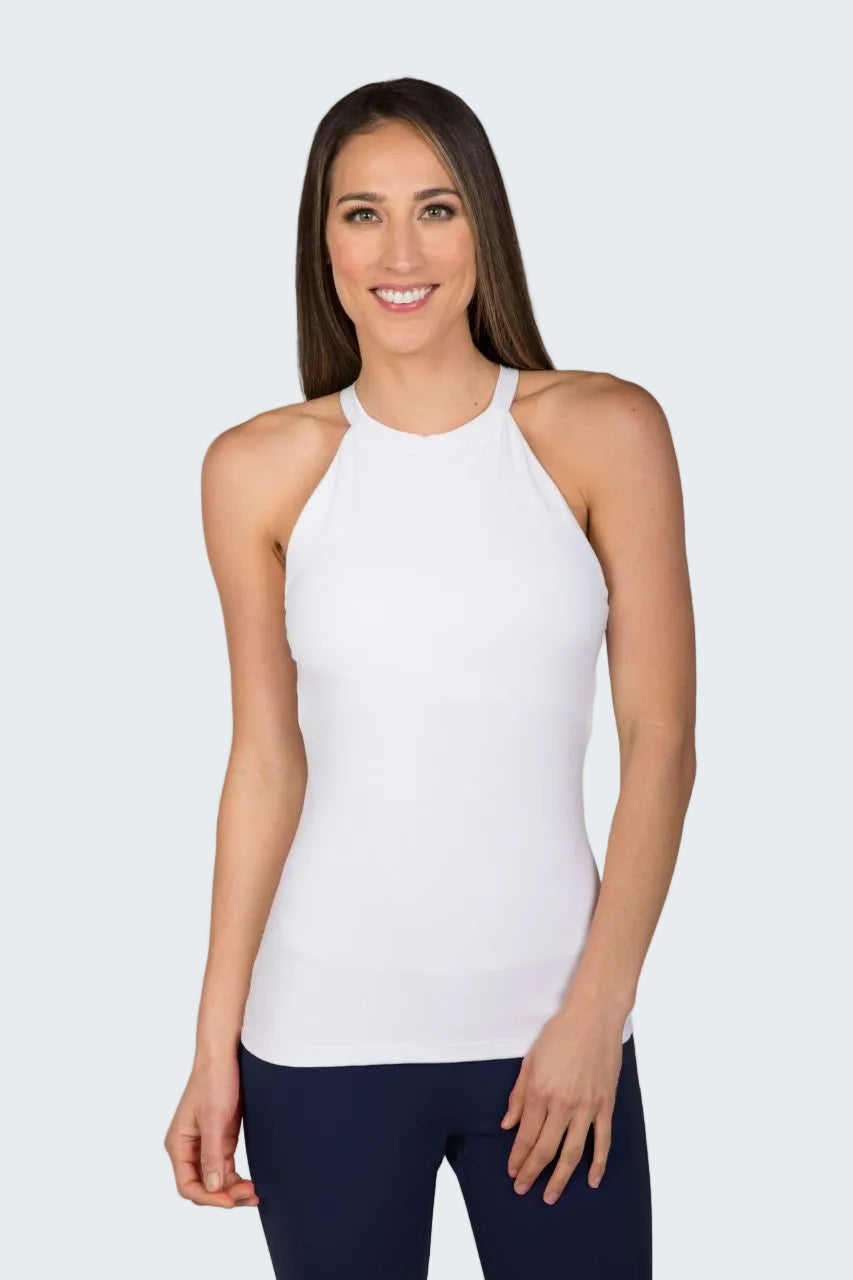 Woman wearing a white sleeveless top and dark pants against a beige background