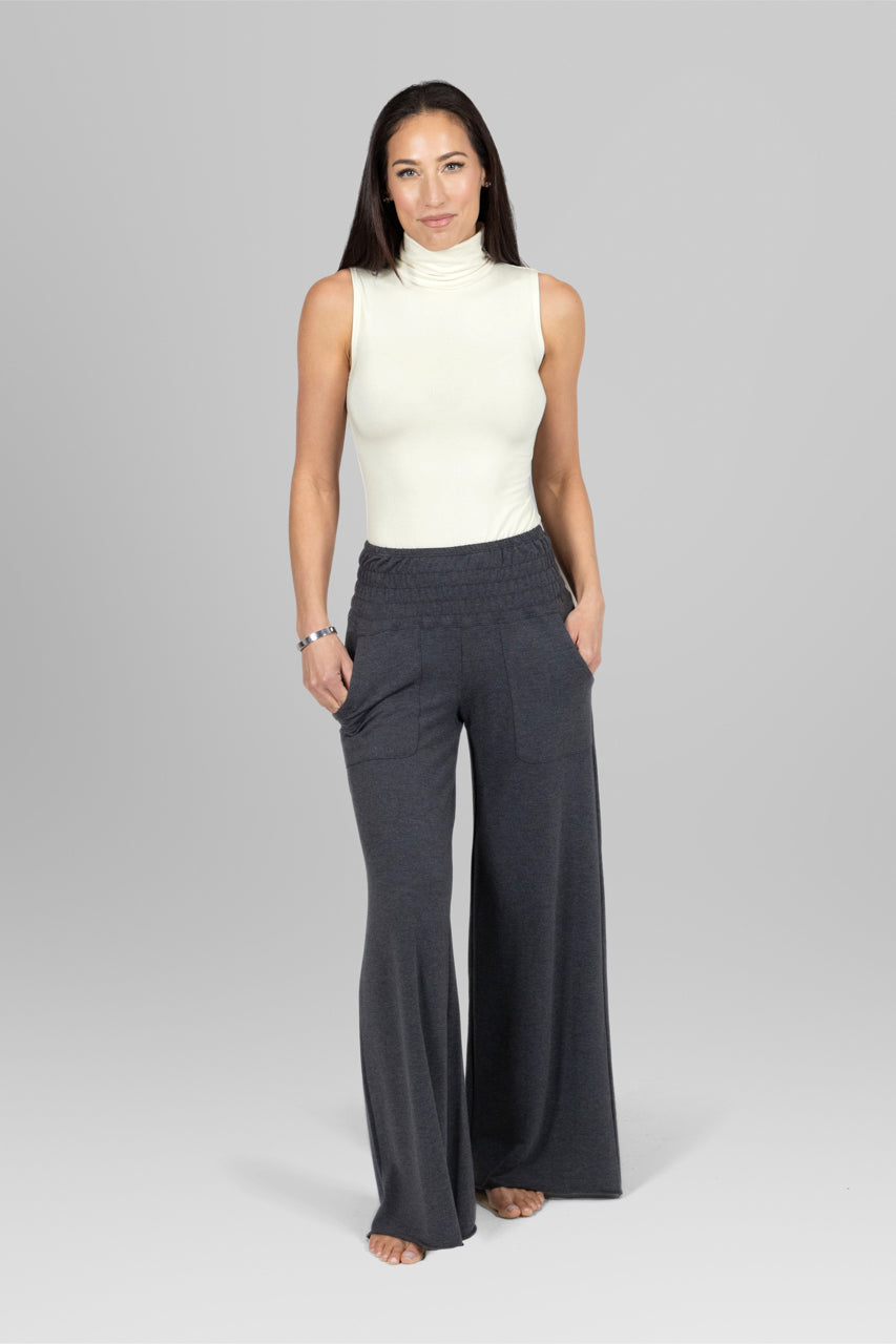 Woman wearing a white sleeveless top and dark gray wide-leg pants on a light gray background