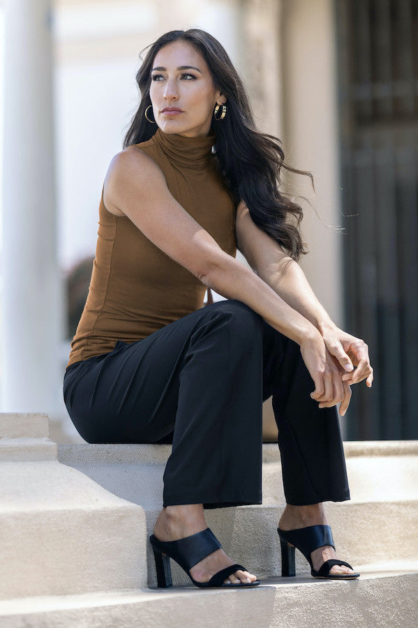 Woman sitting on steps wearing a brown sleeveless top and black pants.