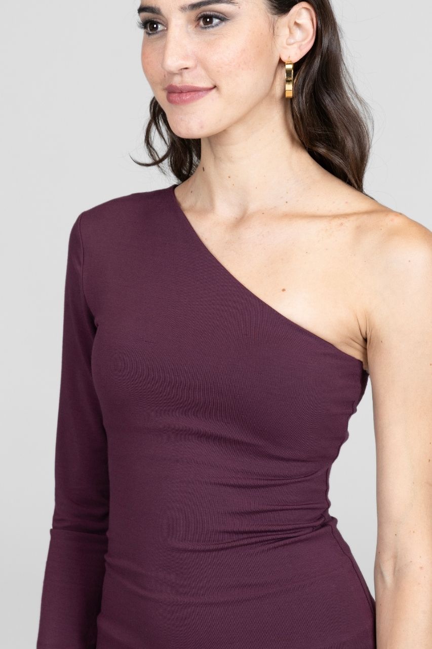 Woman wearing a one-shoulder purple dress against a plain background