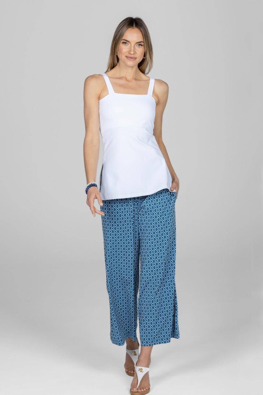 Woman wearing a white tank top and blue patterned pants on a gray background