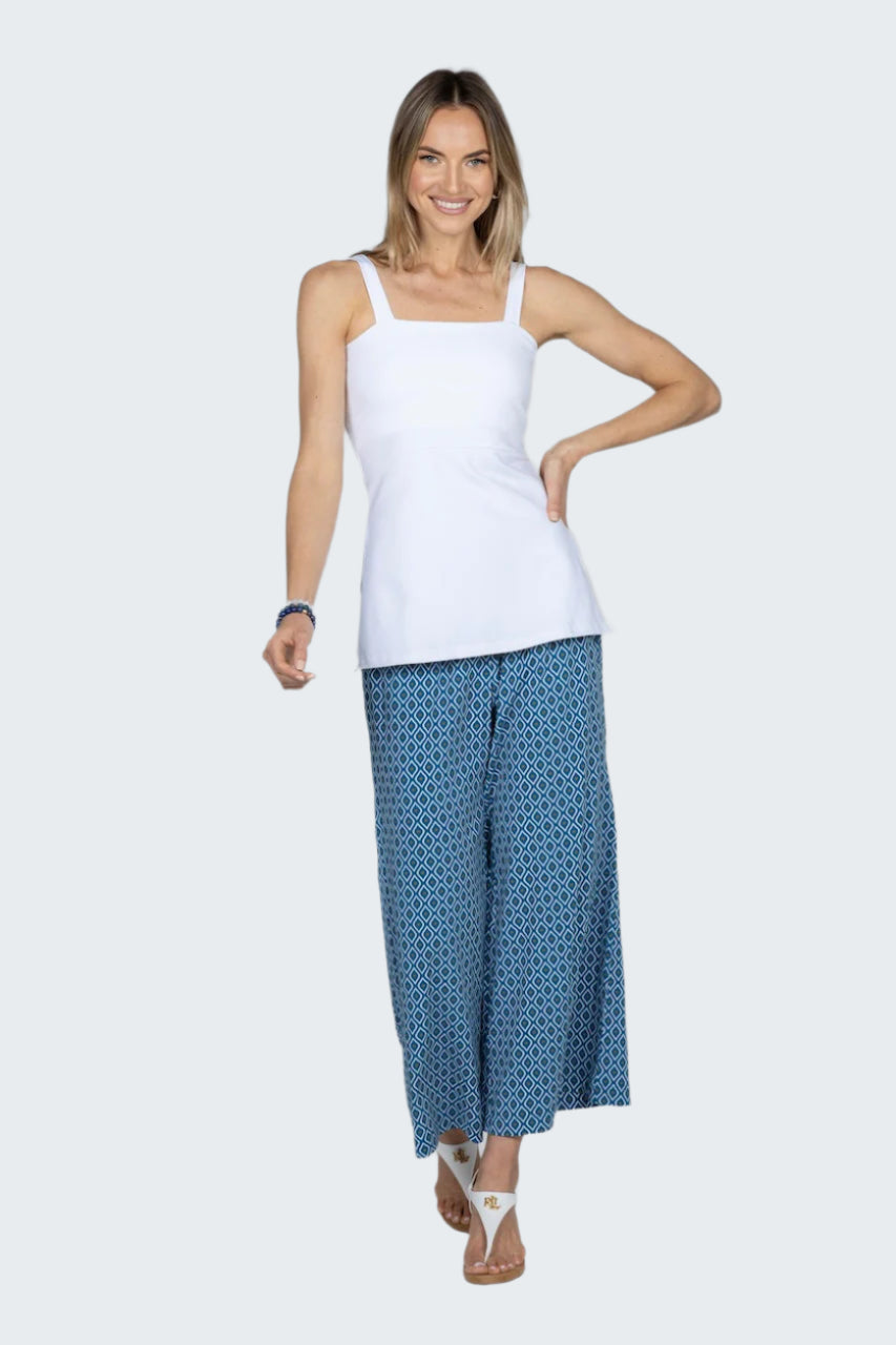 Woman wearing a white tank top and blue patterned pants on a gray background