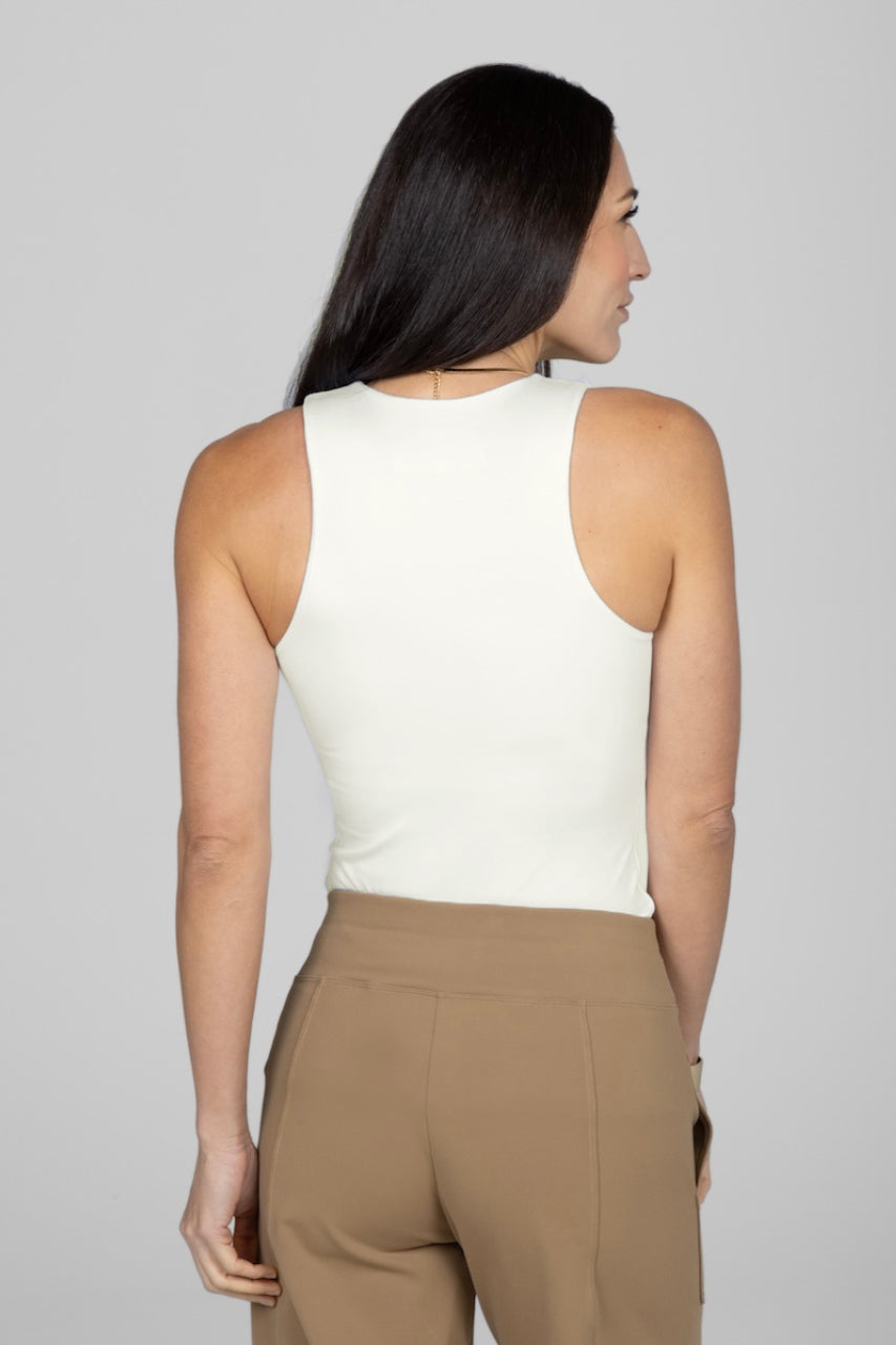 Woman wearing a white sleeveless top and beige pants against a plain background