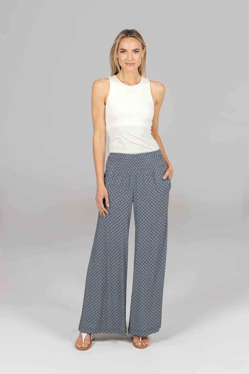 Woman wearing a white sleeveless top and blue patterned pants on a gray background