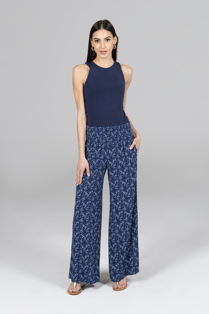 Woman wearing a navy sleeveless top and blue patterned pants on a gray background
