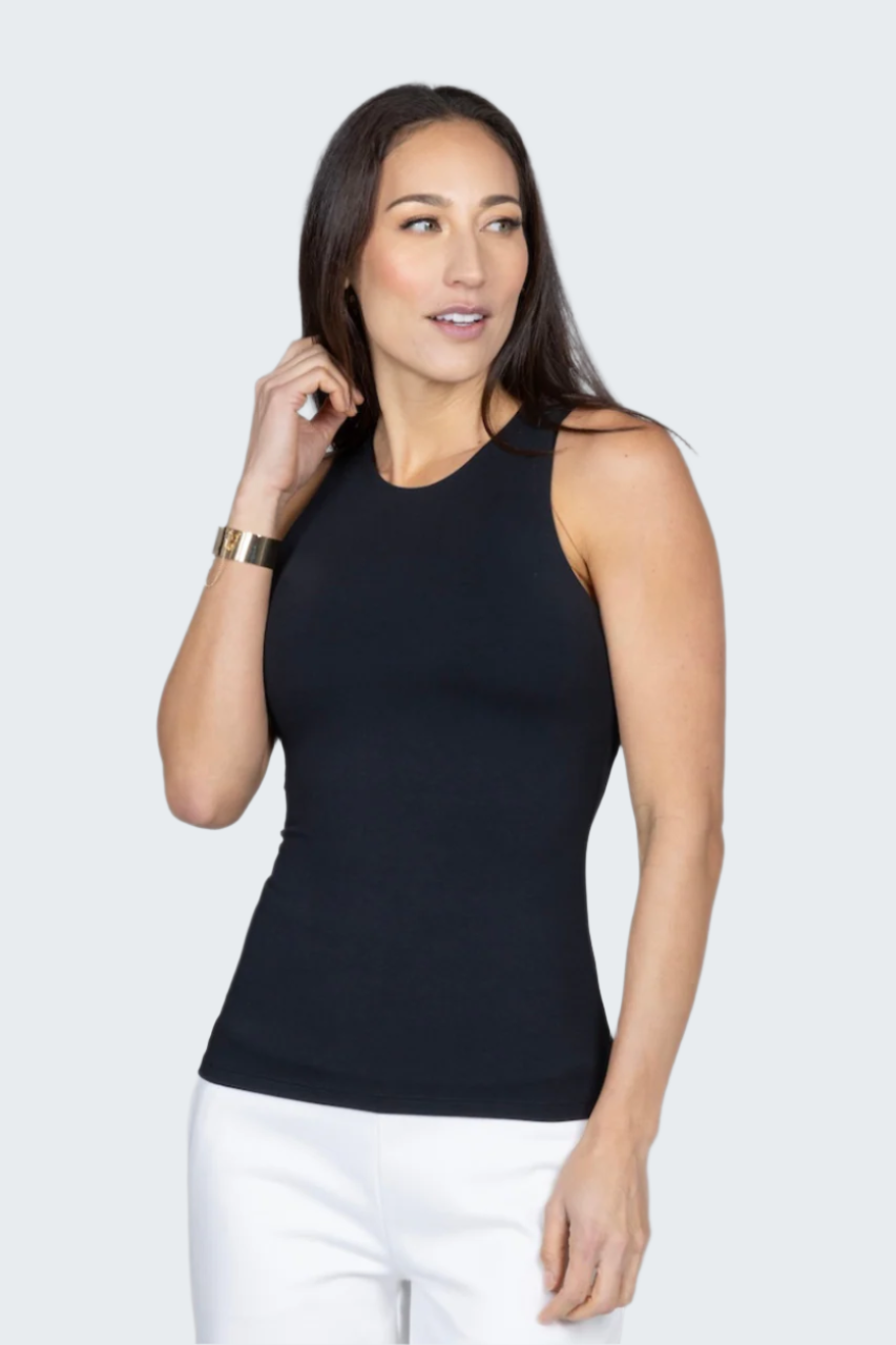 Woman wearing a black sleeveless top and white pants against a gray background