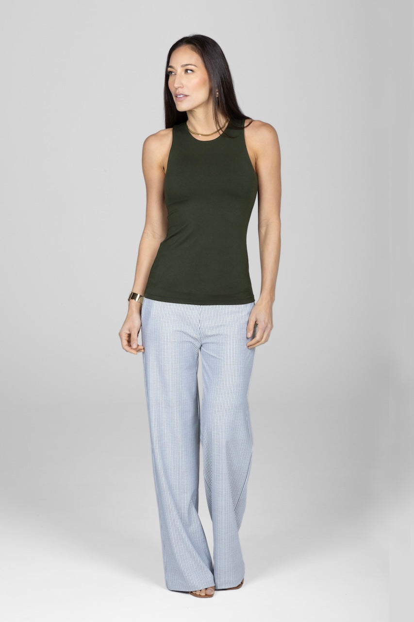 Woman wearing a green sleeveless top and light blue pants on a white background