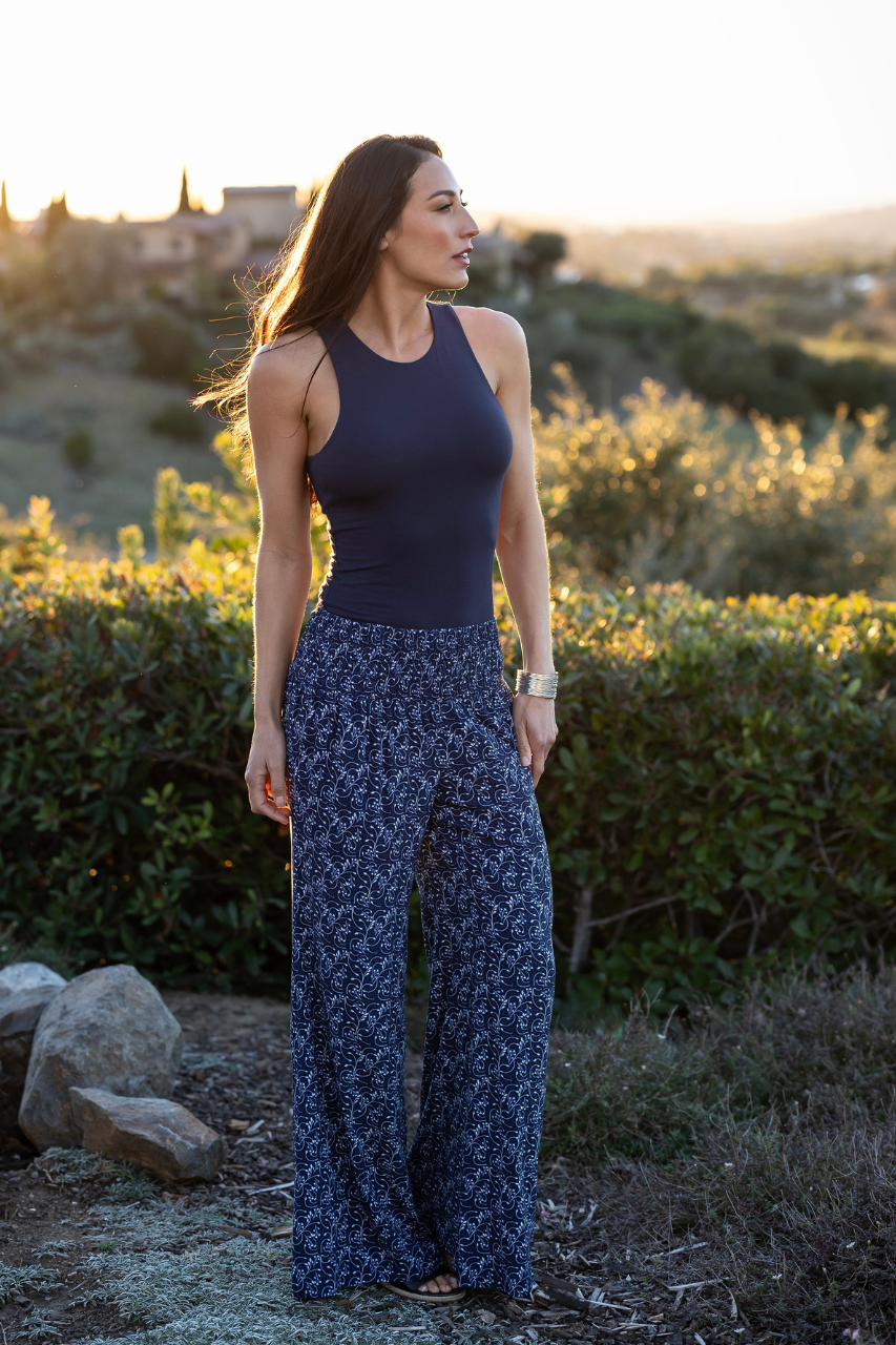 Woman wearing a navy blue top and wide-leg pants standing in a natural setting with greenery and rocks.