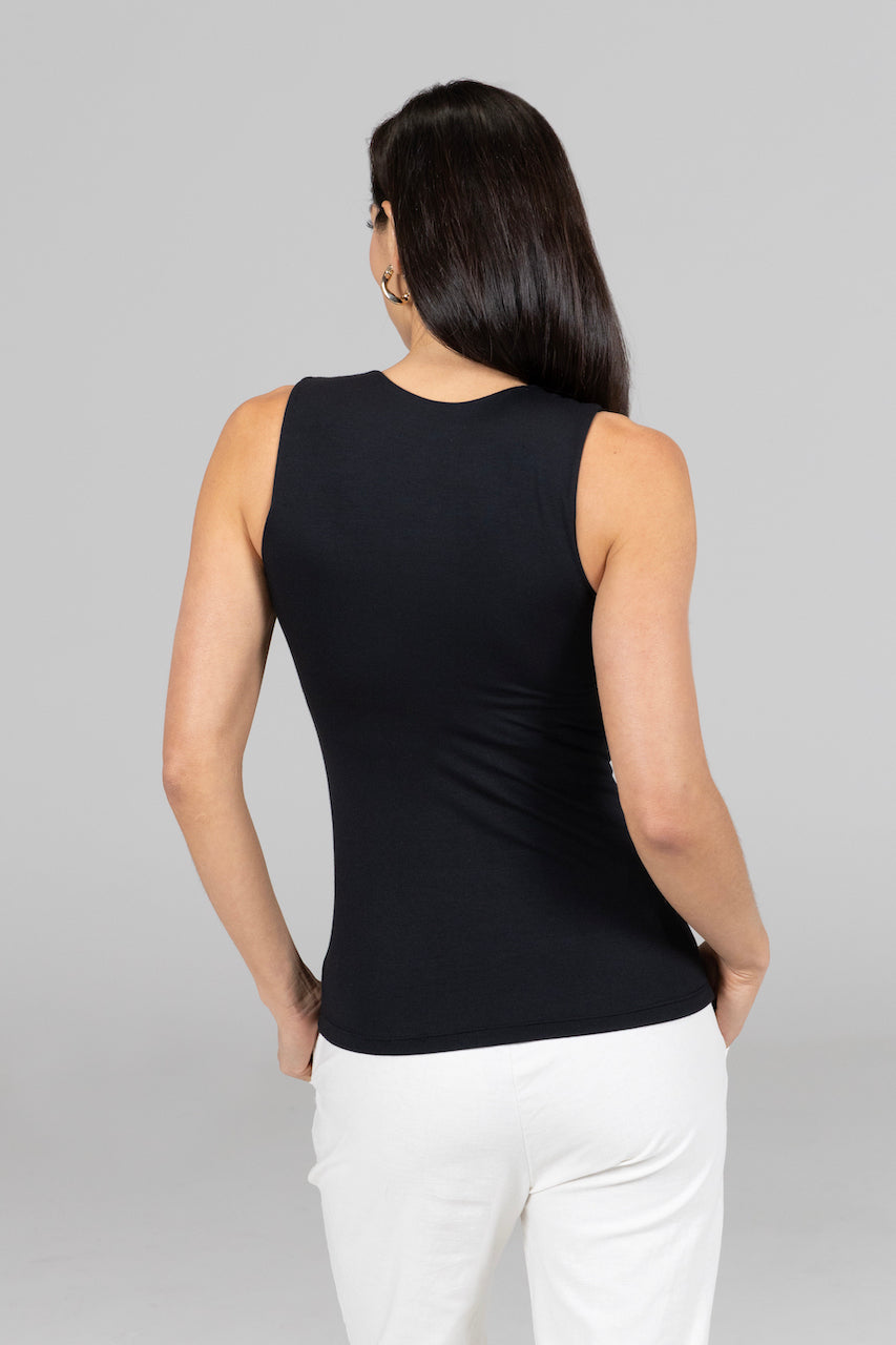 Woman wearing a black sleeveless top and white pants on a gray background