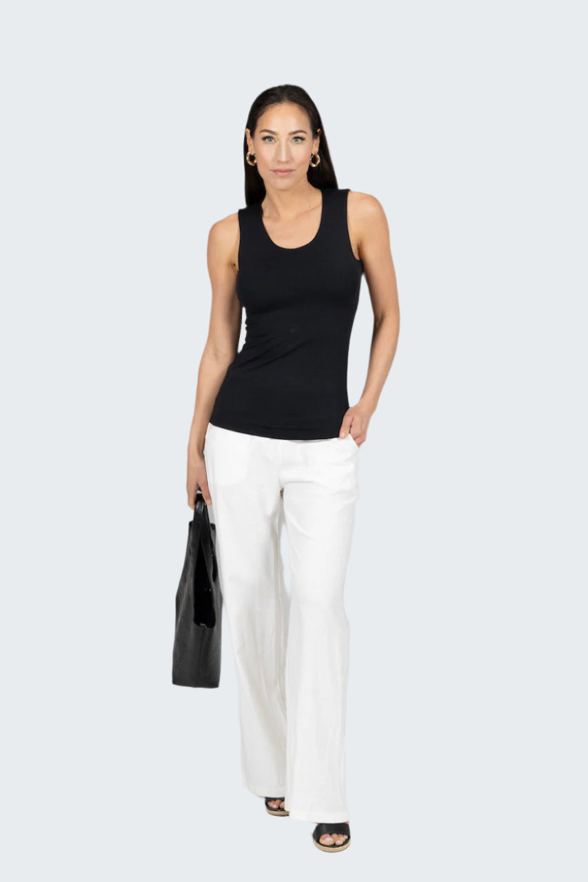 Woman wearing a black sleeveless top and white pants against a gray background