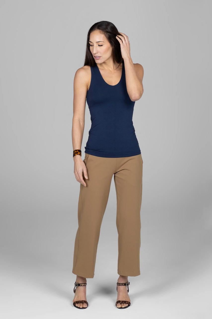 Woman wearing a navy tank top and beige pants on a gray background