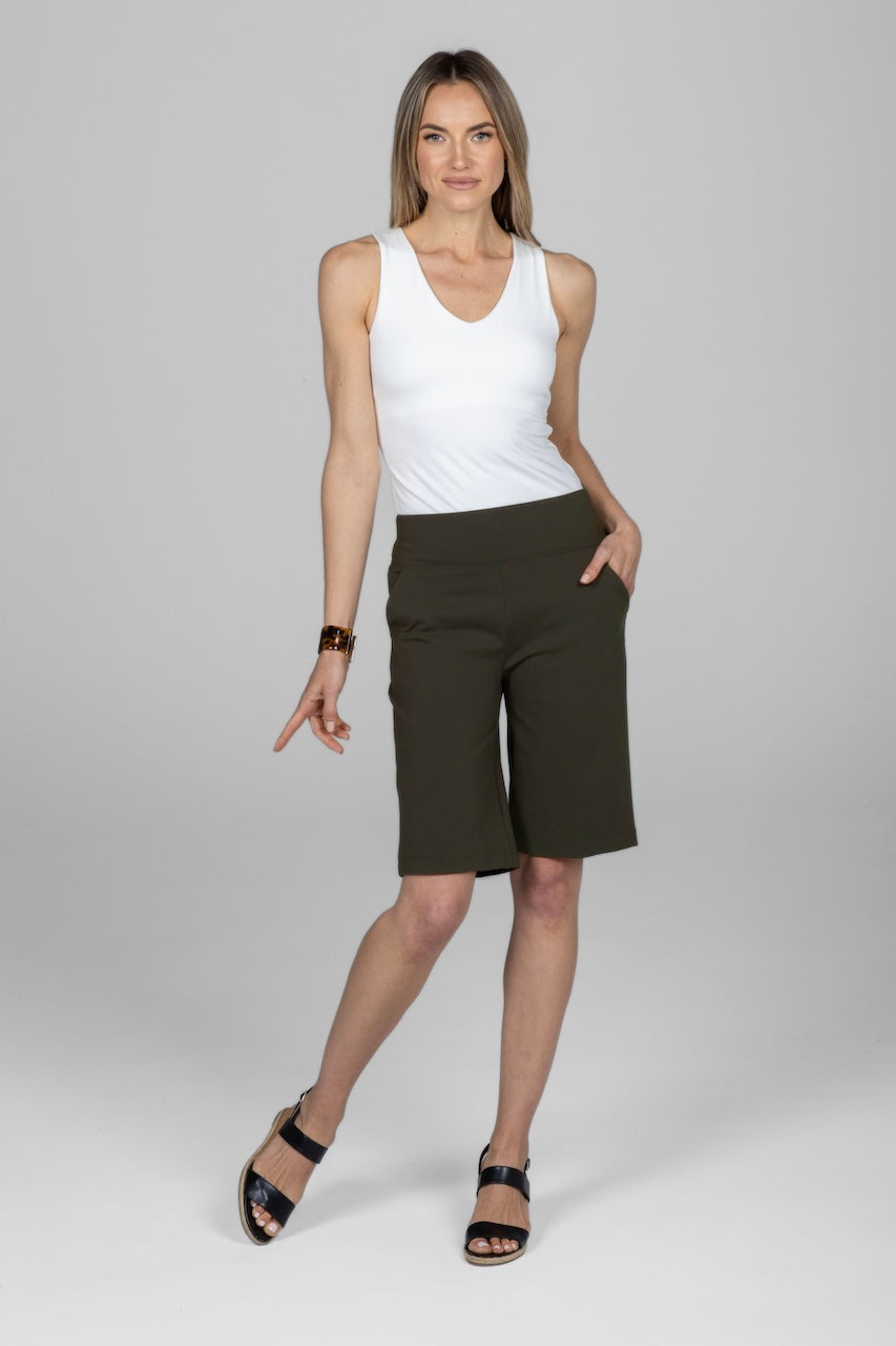 Woman wearing a white tank top and olive green shorts on a gray background