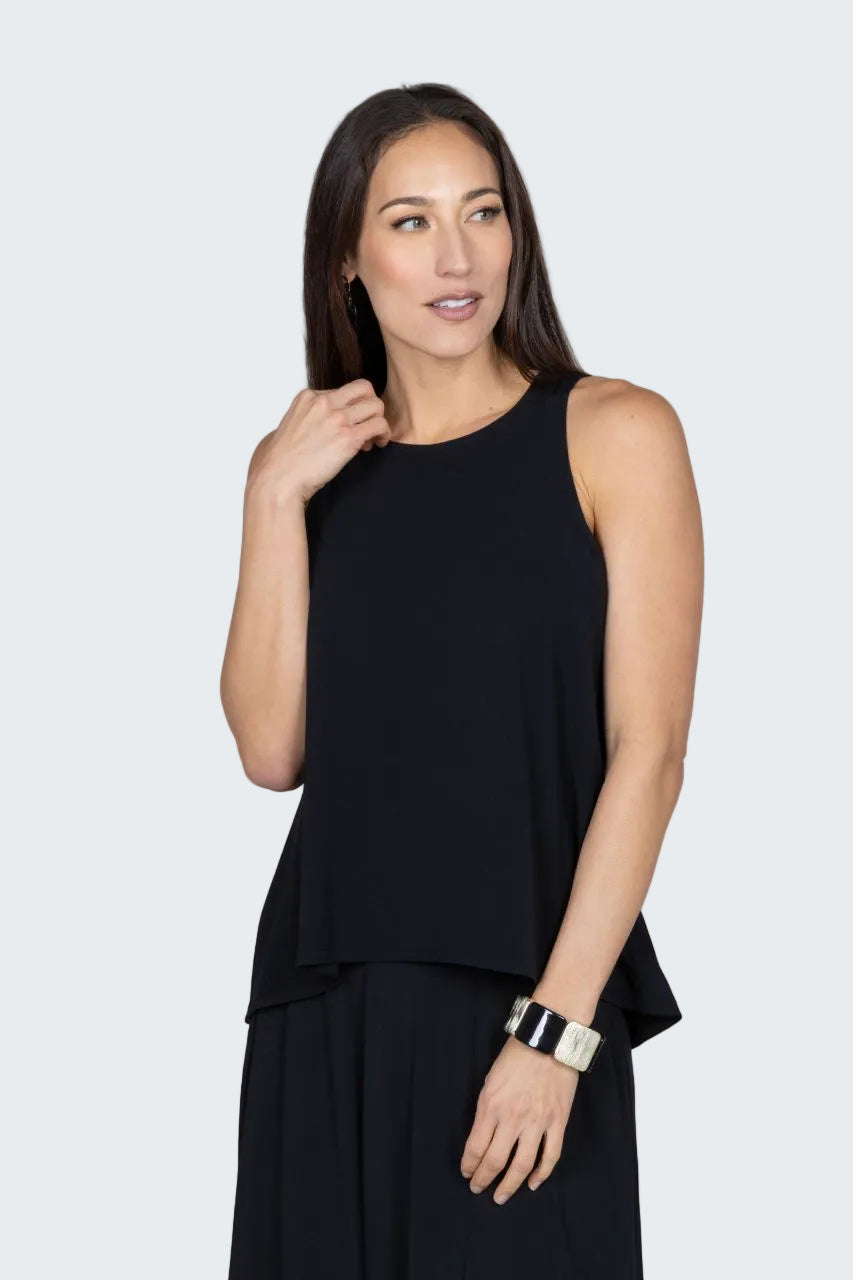 Woman wearing a black sleeveless top and dark pants against a beige background