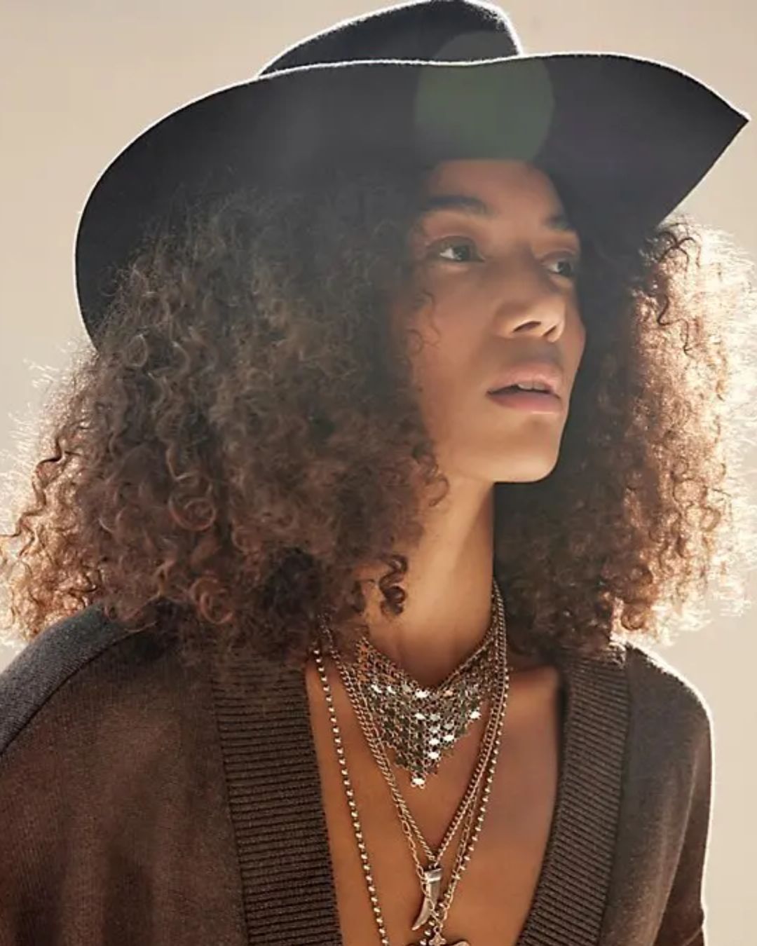 Woman wearing a black hat and layered necklaces against a neutral background
