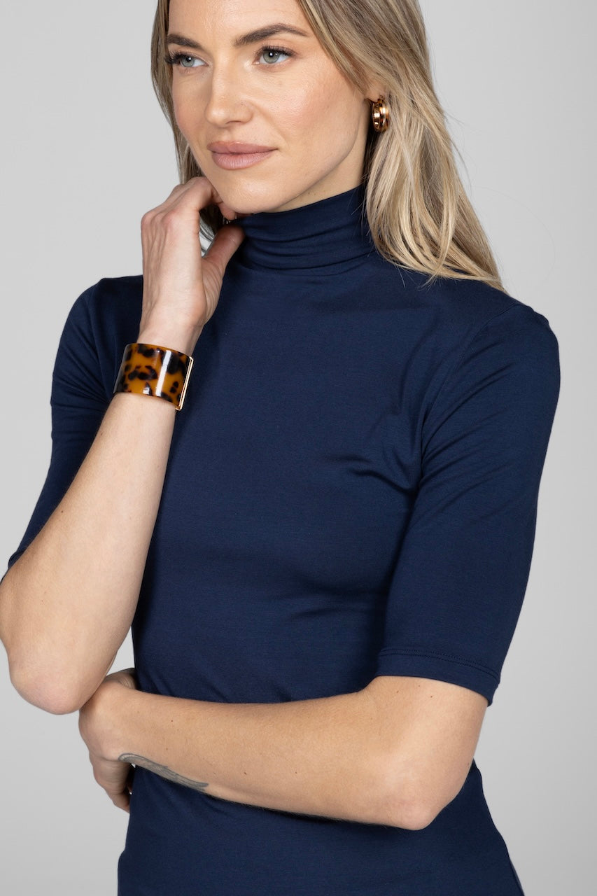Woman wearing a navy blue turtleneck sweater against a plain background