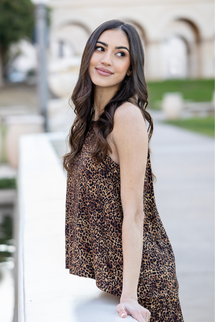 Woman wearing a leopard print dress sitting outdoors.