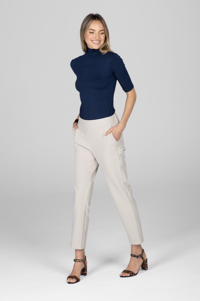 Woman wearing a navy blue turtleneck and beige pants on a white background