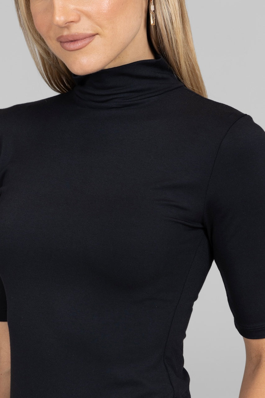 Close-up of a person wearing a black turtleneck shirt against a gray background