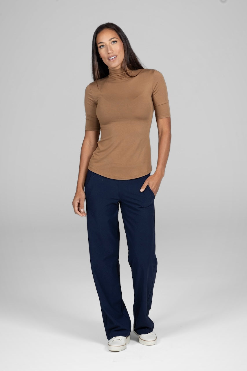 Woman wearing a brown turtleneck and navy pants on a white background