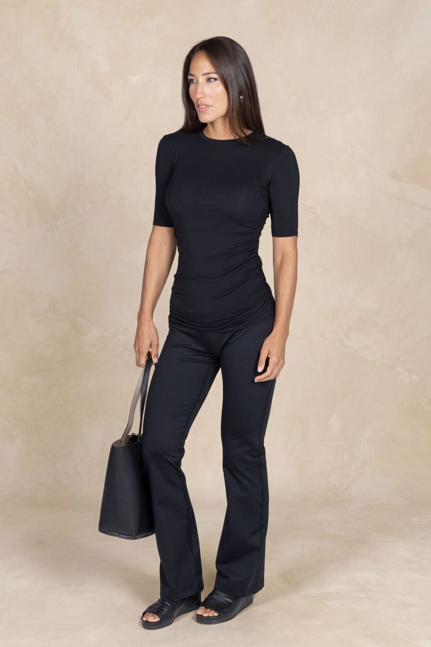 Woman wearing a black outfit holding a black handbag on a beige background