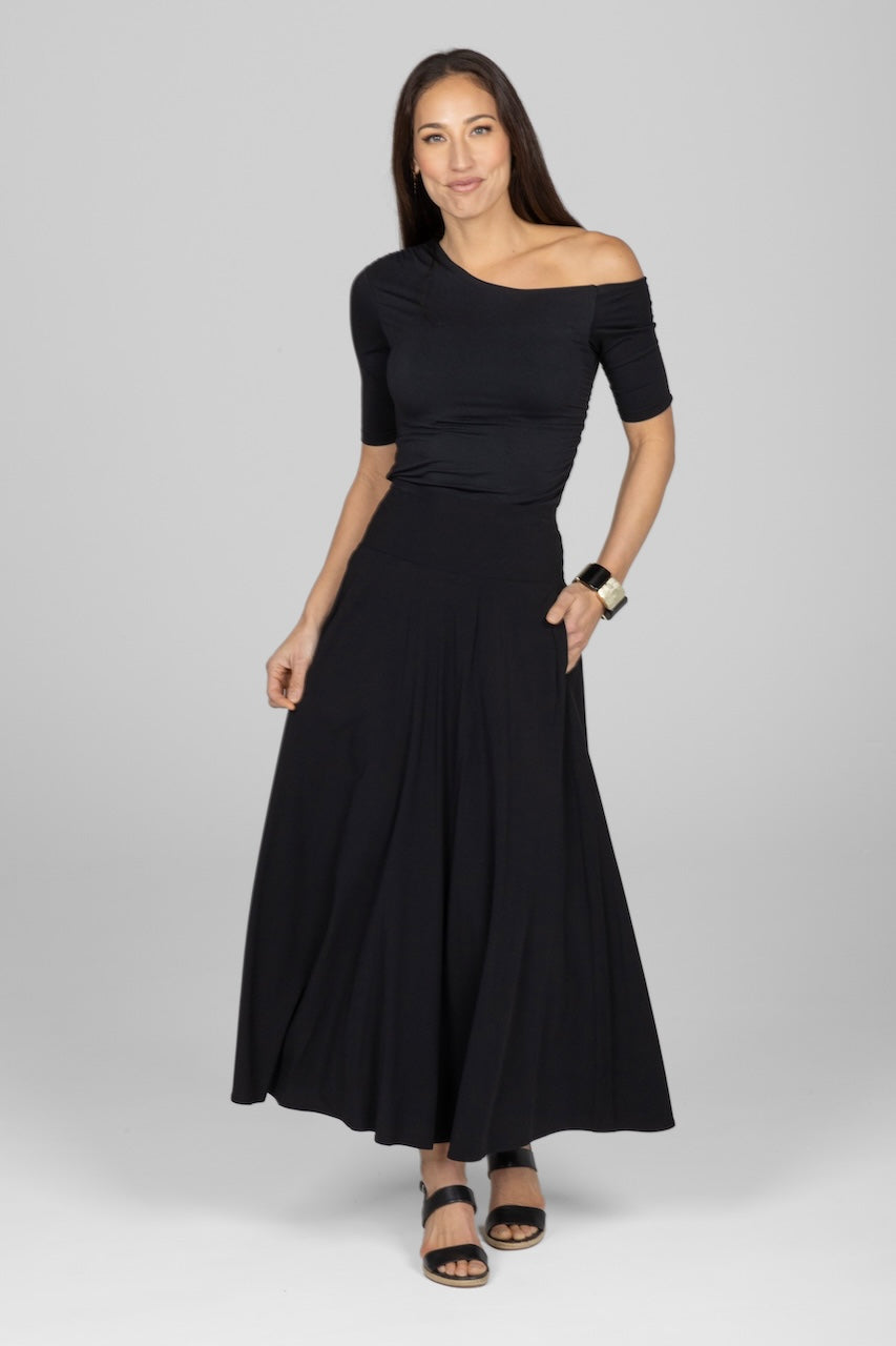 Woman wearing a black off-shoulder top and long skirt on a gray background