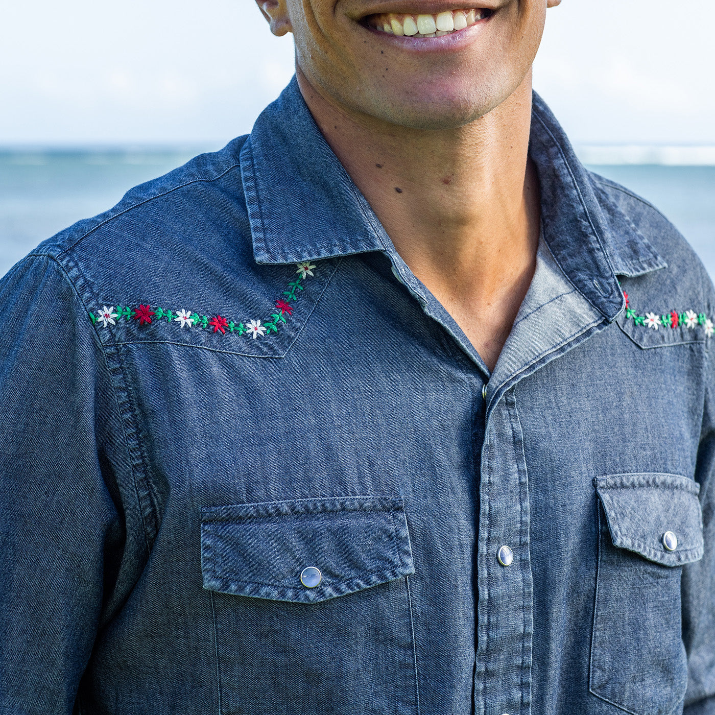 Person wearing a denim shirt with floral embroidery on the sleeves, outdoors.