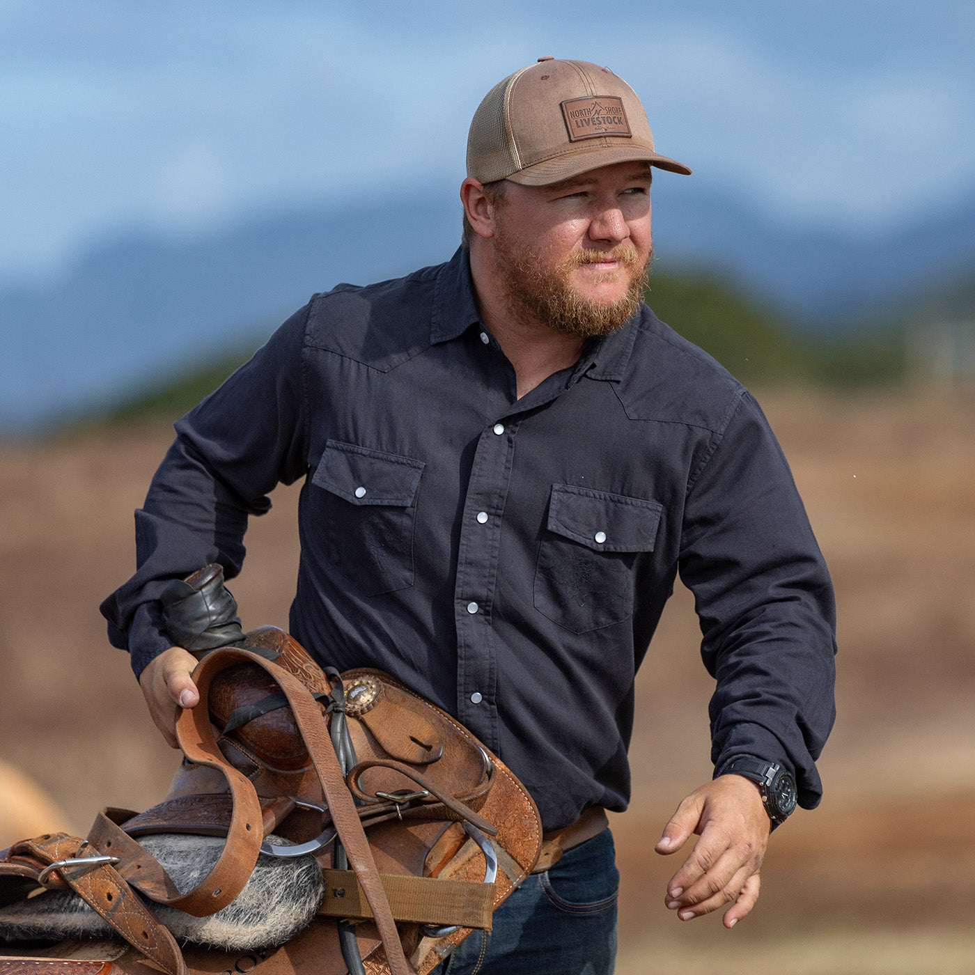 Man holding a saddle in an outdoor setting