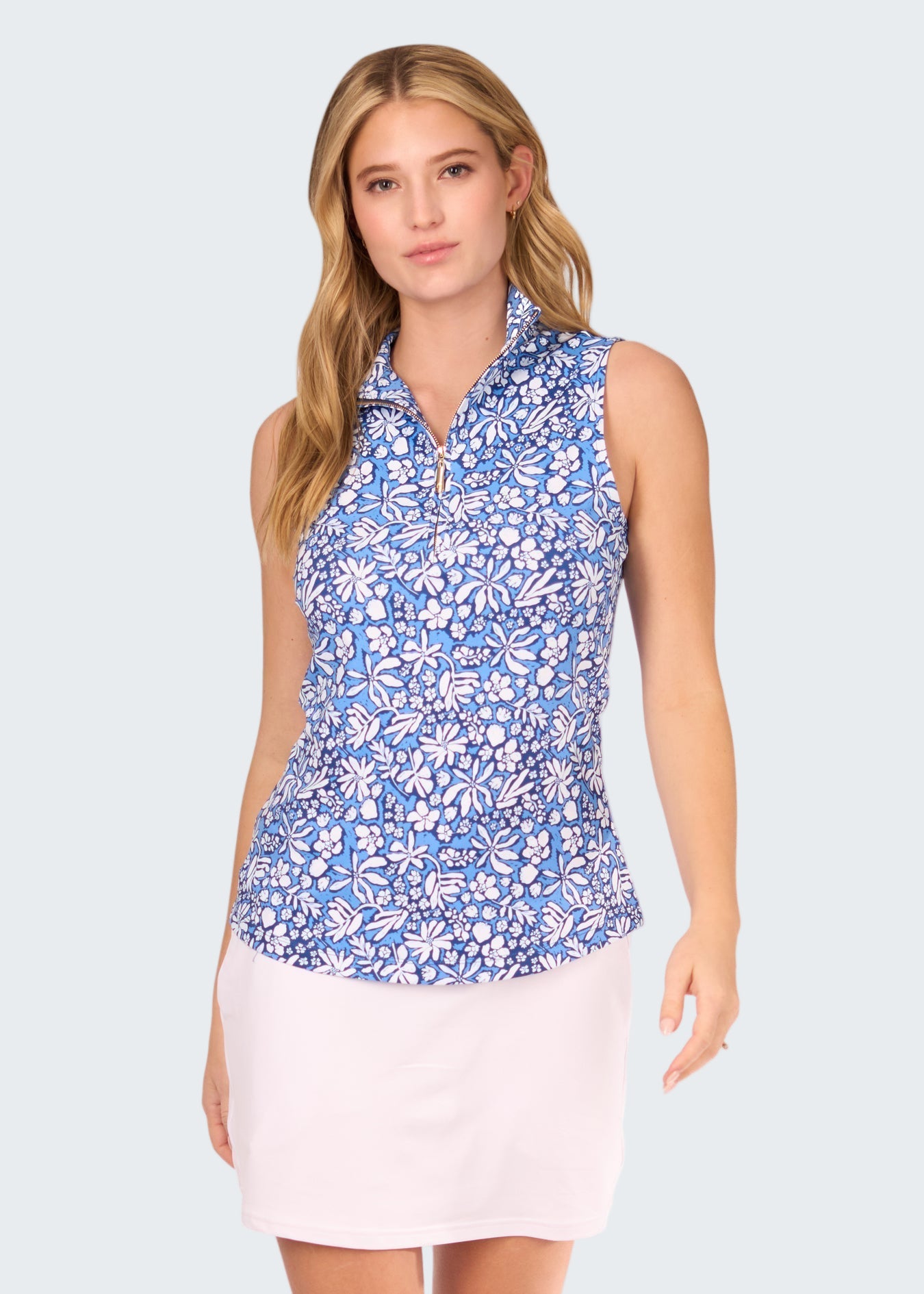 Woman wearing a blue floral sleeveless top and white skirt on a white background