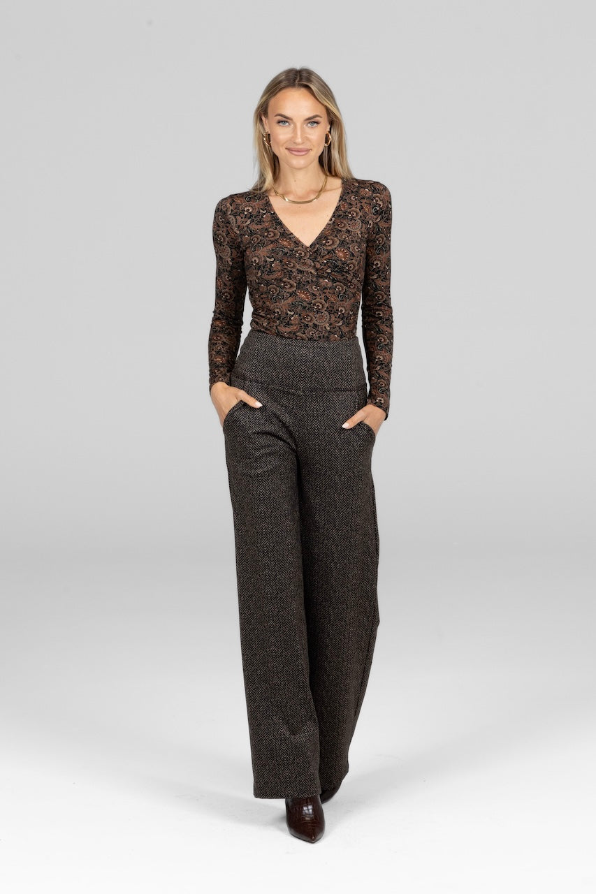 Woman wearing a patterned long-sleeve top and high-waisted pants on a light gray background