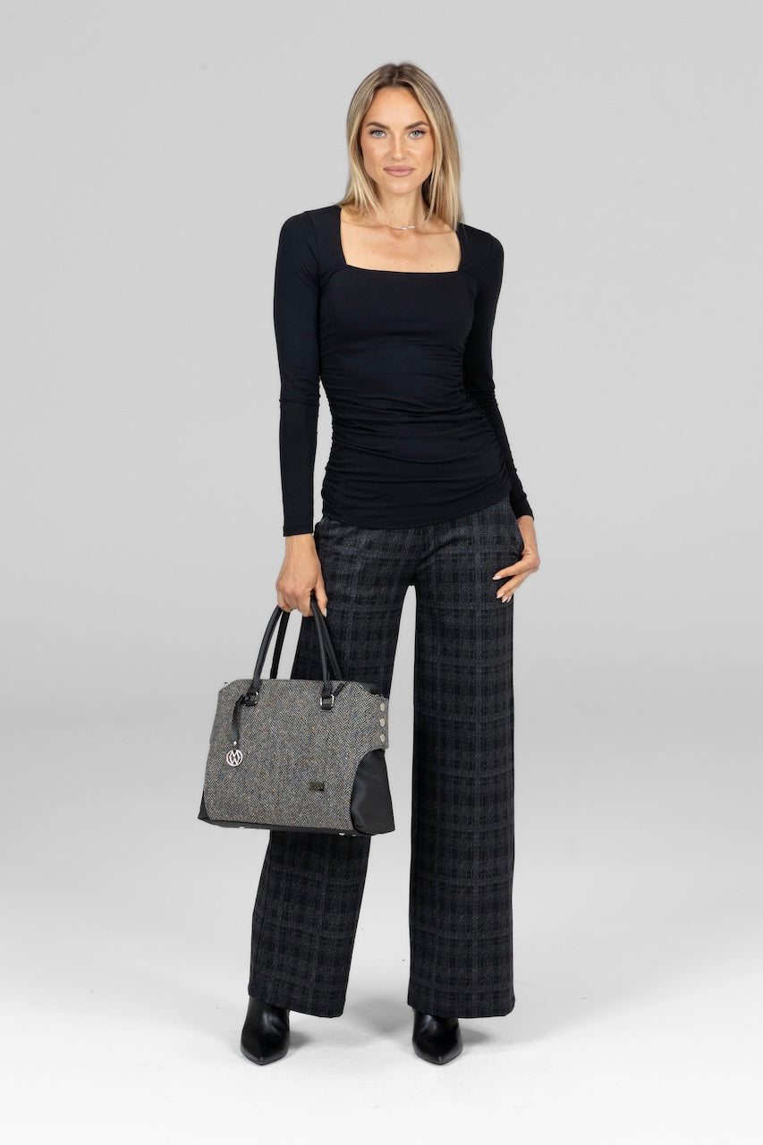 Woman wearing a black top and plaid pants holding a gray handbag on a white background