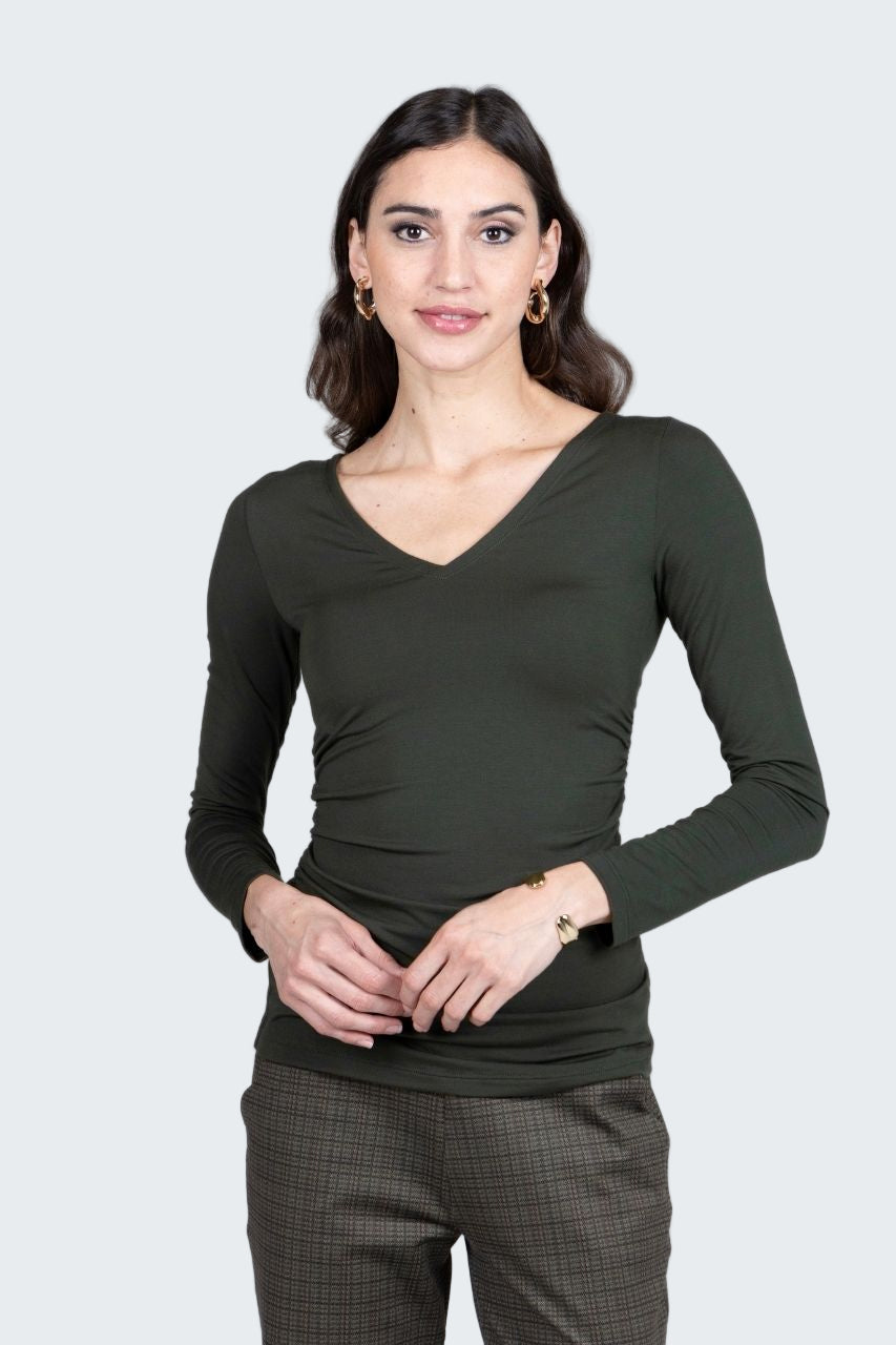 Woman wearing a dark green long-sleeve top and plaid pants on a gray background