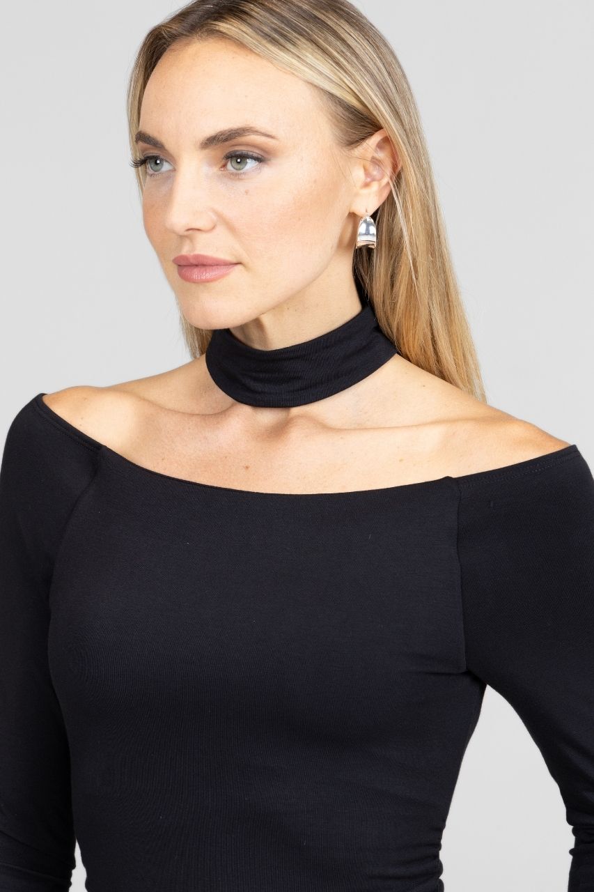 Woman wearing a black off-shoulder top with a high neckline against a gray background