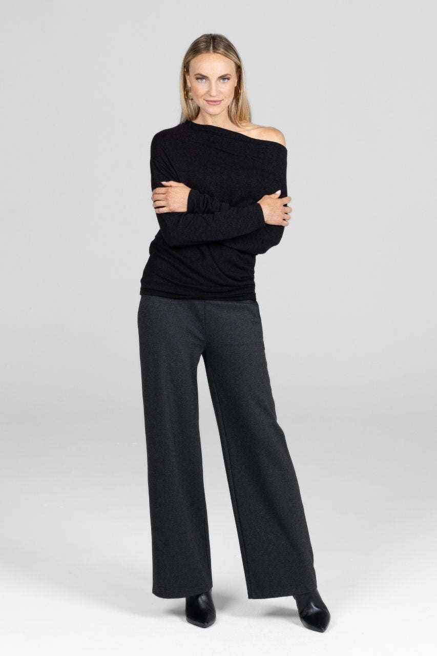 Woman wearing a black off-shoulder top and wide-leg pants on a white background