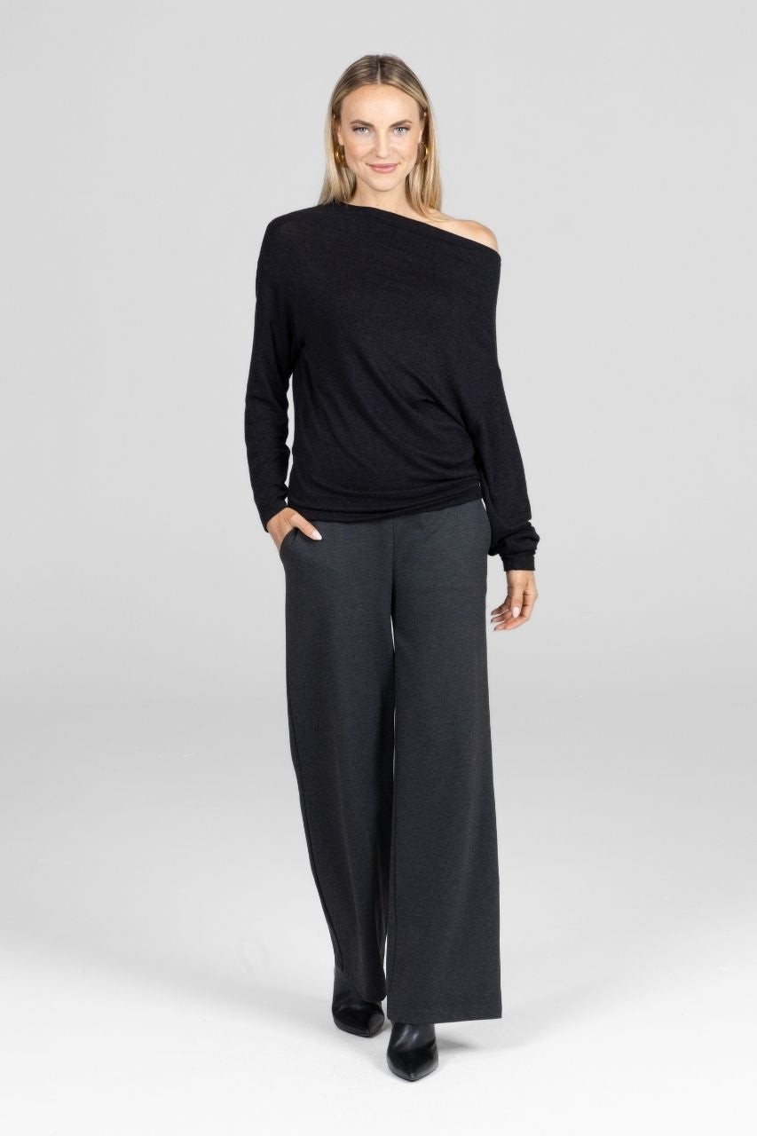 Woman wearing a black one-shoulder top and gray pants on a white background