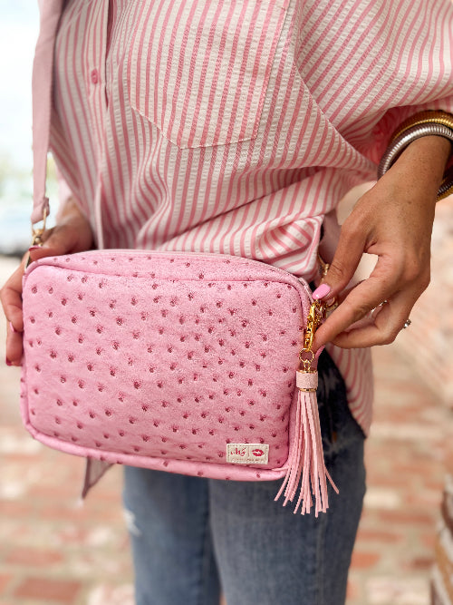 Person holding a pink textured handbag with tassel detail.