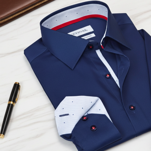Folded navy blue dress shirt with white collar and red buttons on a light wooden surface, next to a pen.