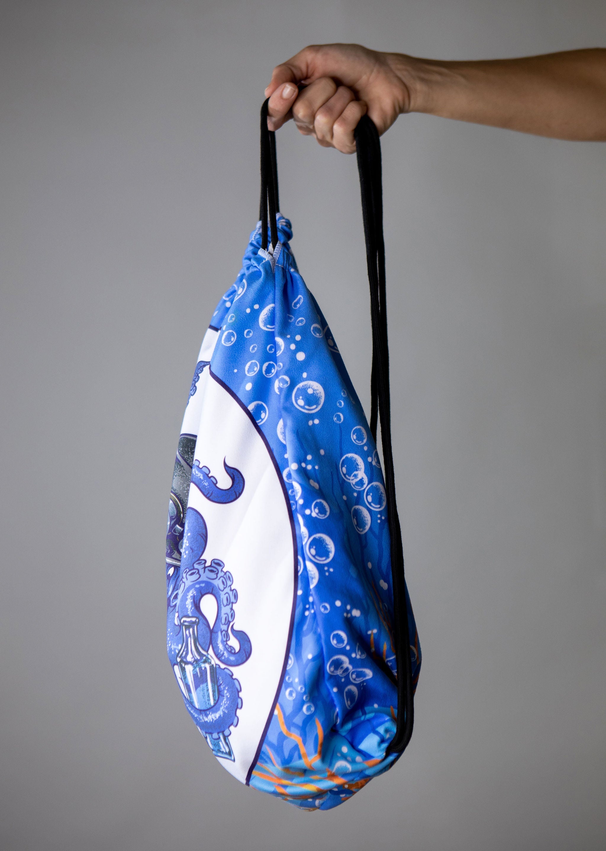 Blue drawstring bag with white design held by a hand against a gray background
