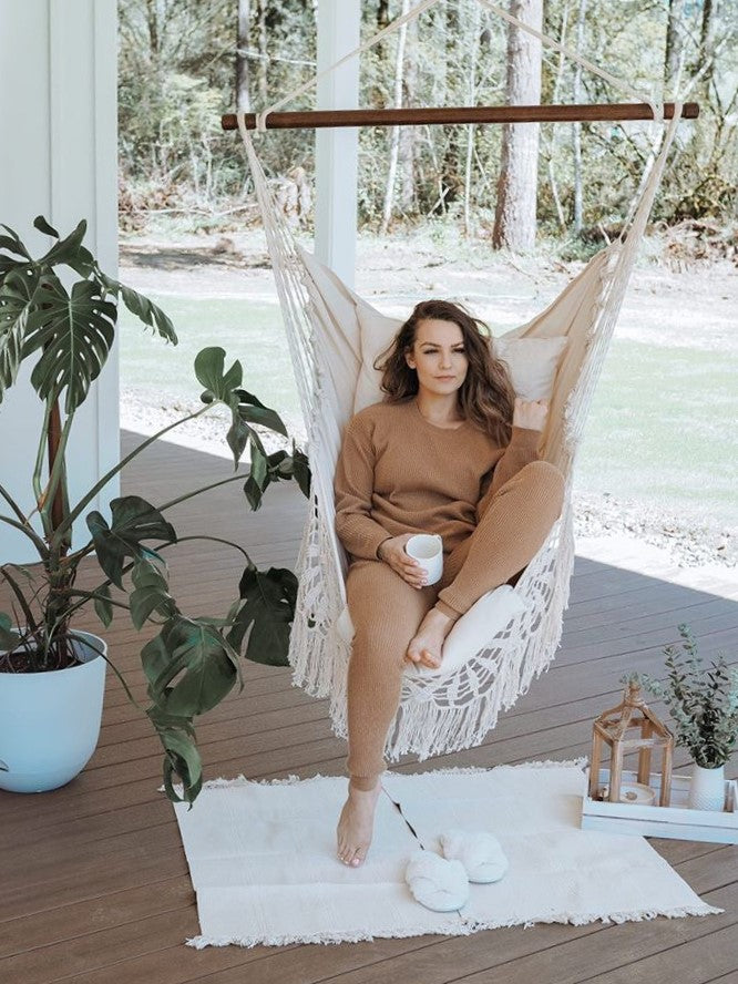 Woman sitting in a hammock on a wooden deck with plants and decor around her.