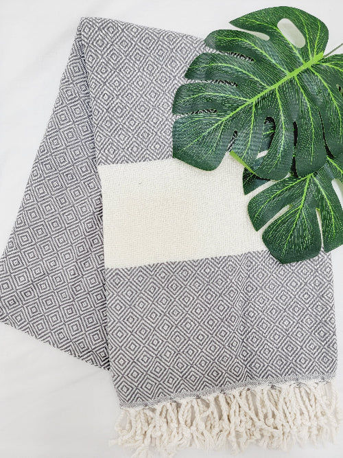 Gray geometric patterned towel with white border and fringes, featuring a green leaf on a white background.
