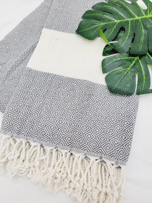 Gray and white patterned towel with fringes on a surface with a green leaf.