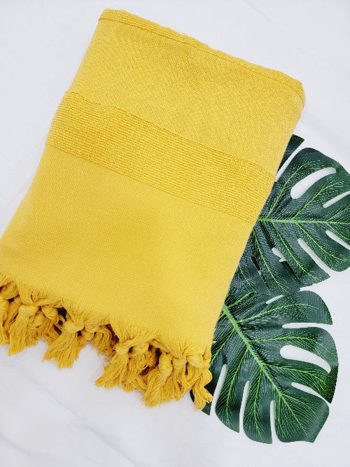 Yellow towel with tassels on a white background with green leaves.