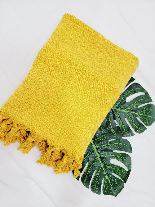 Yellow towel with fringes on a white background with green leaves.
