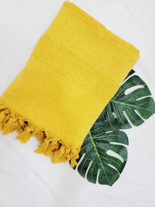 Yellow towel with fringes on a white background with green leaves.