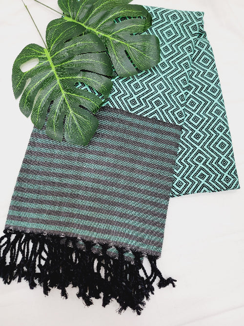 Striped towel with tassels and a patterned green fabric on a white background